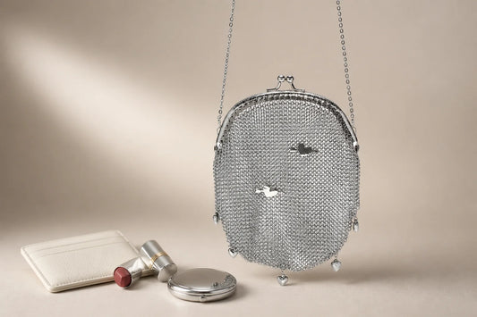 Silver stainless steel mesh clutch purse on a warm studio backdrop with evening essentials