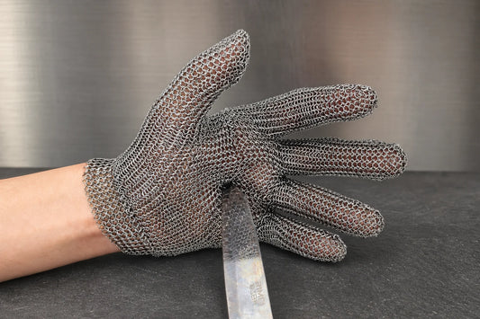 Stainless steel mesh butcher glove holding a knife on a dark slate bench