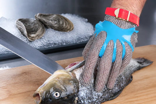 Five-finger stainless steel mesh glove gripping a fish at a seafood prep station with oysters on crushed ice