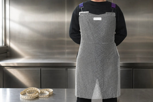 Stainless steel chainmail apron in a prep kitchen with a coiled measuring tape on the counter