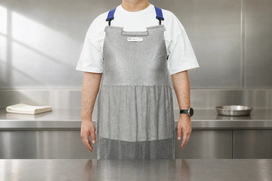 Stainless steel chainmail apron worn in a professional kitchen with a folded cloth and basin on the counter
